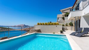 Un espace piscine moderne offrant une vue dégagée sur la mer et un paysage montagneux en arrière-plan.