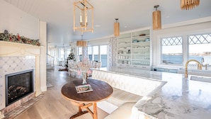A spacious living area with a fireplace, a round wooden table, and a large window overlooking the ocean. - Luxury oceanfront 5 bedroom, 5.5 bath private dock overlooking Mothers Beach! (Kennebunk)