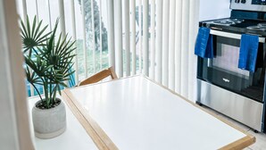 A modern kitchen with a white table, a potted plant, and a view through large windows.