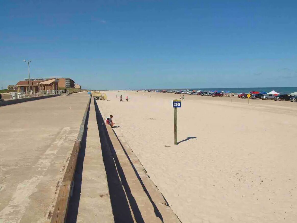 A beach with a concrete walkway, a signpost, and a building in the background.