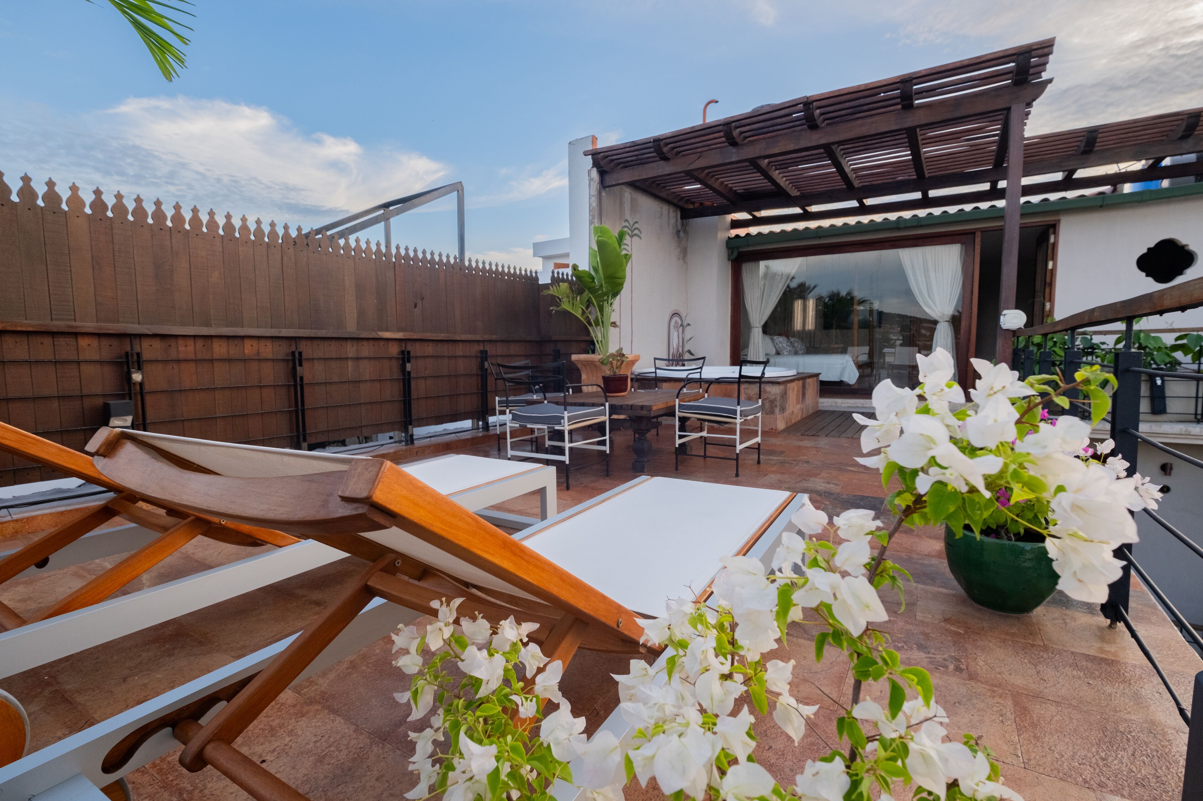 A rooftop patio with wooden lounge chairs, a table, and potted plants.
