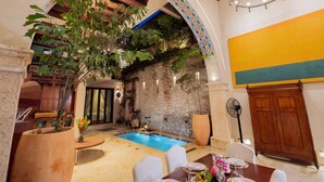 A pool area with a stone wall, a wooden ceiling, and a dining table with chairs. - Luxury 5BR House W Jacuzzi & Pool (Cartagena)
