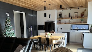 A modern living room with a leather sofa, a dining area with a wooden table, and a kitchen with white cabinets and a black refrigerator.