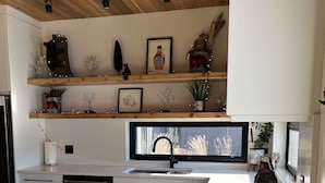 A modern kitchen with white cabinetry, a black dishwasher, a wooden ceiling, and a window overlooking a garden.