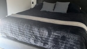 A bedroom with a dark headboard, a bed with grey bedding, and a wooden floor.