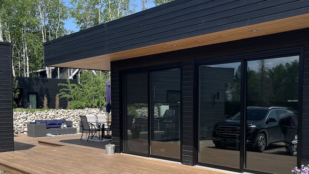 A modern house with a wooden deck, outdoor seating, and a car visible through the glass doors.