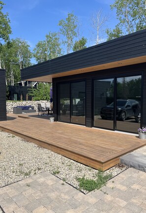 Een modern huis met een houten terras, buitenmeubels en een auto zichtbaar door de glazen deuren.