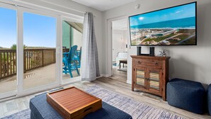 A spacious living area with a large sliding glass door leading to a balcony, a flat-screen TV mounted on the wall, and a wooden cabinet with drawers. - La Mirage Condo 112 Beachfront Resort Condominiums with Private Boardwalk (Port Aransas)