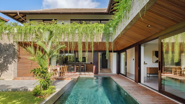 A modern house with a swimming pool, wooden deck, and indoor seating area.