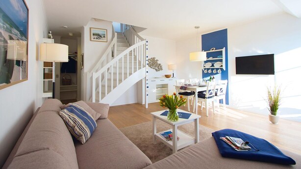 A modern living room with a staircase, a dining area, and a TV mounted on the wall.