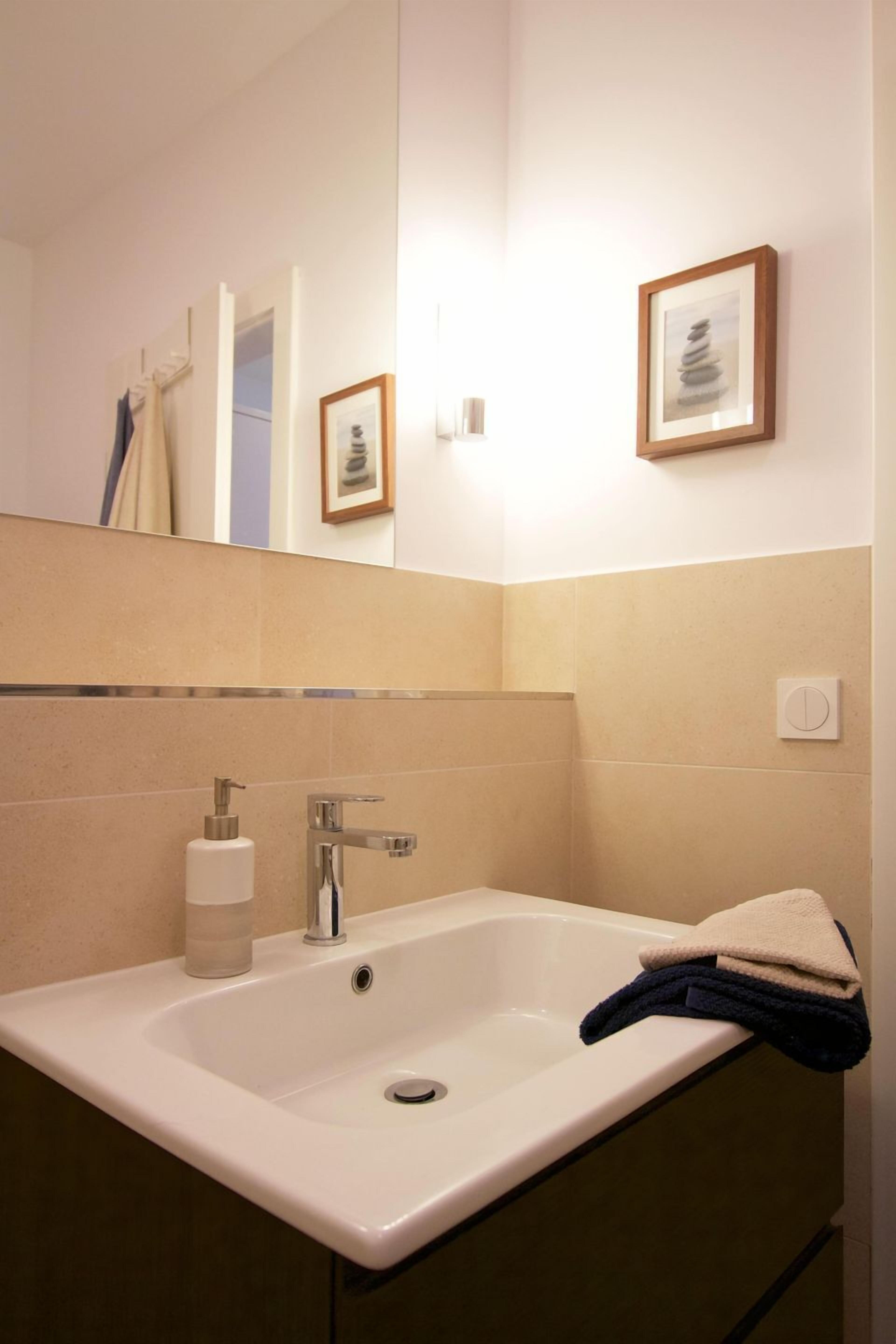 Un baño con un lavabo blanco, un espejo y un cuadro en la pared.