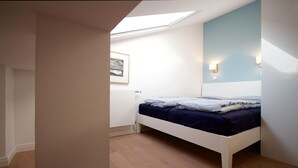 A bedroom with a skylight, a bed, a wall-mounted light, and a framed picture.