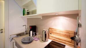 A compact kitchen with a sink, a coffee maker, a toaster, and a wooden cutting board.