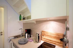 A compact kitchen with a sink, a coffee maker, a toaster, and a wooden cutting board.