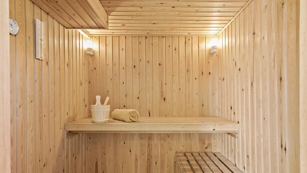 Ein Saunaraum mit Holzwänden, einer Sitzbank, einem Ablagebereich mit Handtüchern und einem Wandheizgerät.