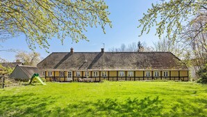 Ein traditionelles Gebäude mit einem geneigten Dach, einem kleinen Garten davor und wolkenlosem, blauem Himmel.
