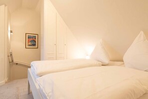 Une chambre avec deux lits simples, un tableau encadré au mur et une porte blanche.