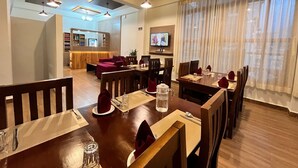 A modern dining area with wooden tables and chairs, a kitchen in the background, and a TV mounted on the wall. - Norbu Healing Hotel (Thimphu)