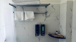 A bathroom with a marble wall, a towel rack with folded towels, and two shampoo bottles. - Norbu Healing Hotel (Thimphu)