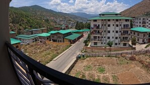 A view of a residential area with multiple buildings, a road, and a mountainous backdrop. - Norbu Healing Hotel (Thimphu)