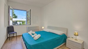 A bedroom with a bed, a chair, a nightstand, a lamp, and a window with an open view. - La Primula Apartment 2 with Sea-View, Salve, Italy (Salve)