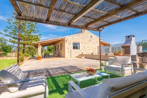 Un patio al aire libre techado con paredes de piedra, una parrilla y mobiliario exterior.