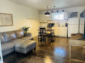 A compact living space with a gray leather sofa, a dining table with chairs, a small kitchen area with a microwave, and a refrigerator. - #5 Hidden Akers -Peaceful, quiet, safe, relax, enjoy,country life. Pet friendly. (Folsom)