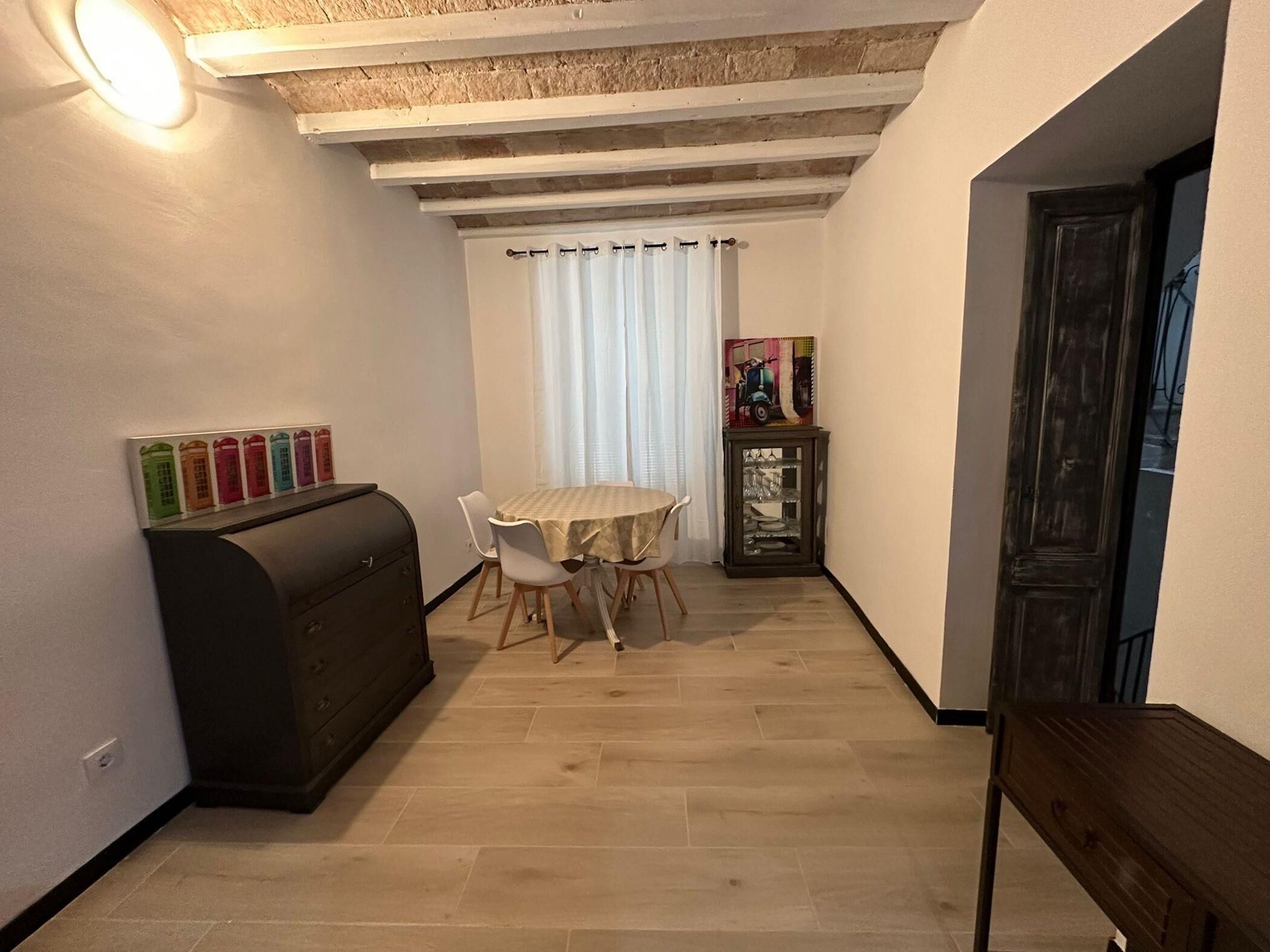 Ein schmaler Flur mit Esstisch und Stühlen, einem dunklen Schrank und einer Tür auf der rechten Seite.