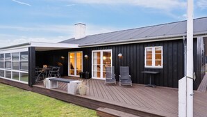 Ein modernes Haus mit Terrasse, großen Fenstern und Grillplatz.