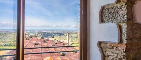 A room with a large window overlooking a tiled roof and a distant landscape.