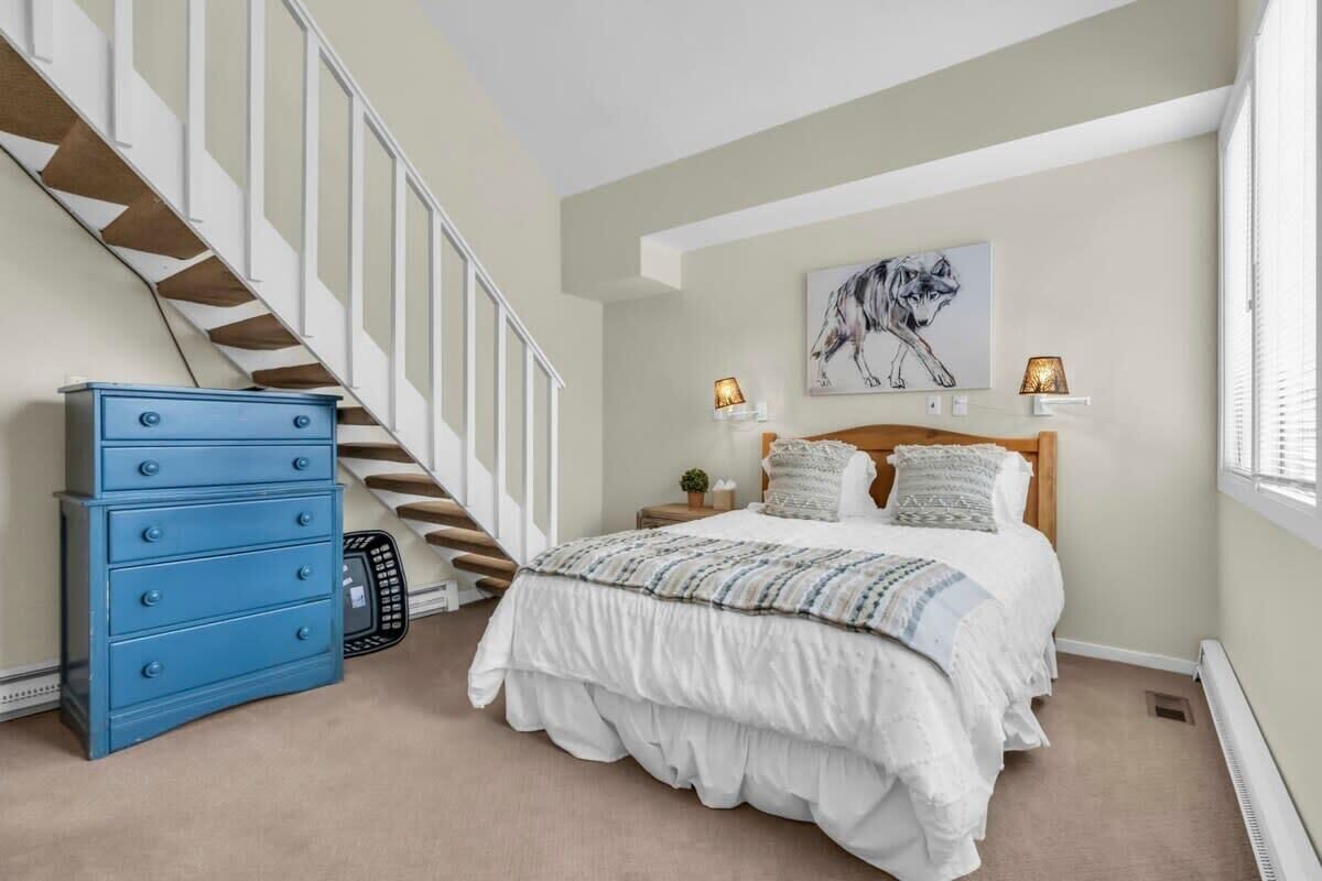 Un dormitorio con cama, cómoda, escalera y una lámpara de pared.