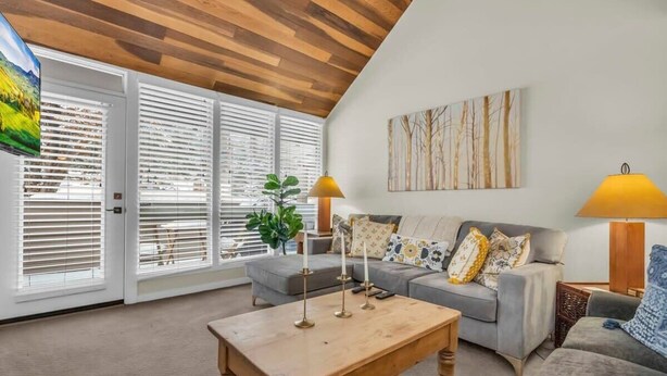 Ein Wohnzimmer mit Holzboden, einem grauen Sofa, einem Holztisch und zwei Lampen.