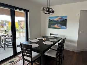 A dining area with a black table, six chairs, and a painting of a landscape on the wall.