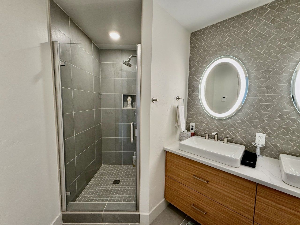 Un baño moderno con ducha, tocador y dos espejos.