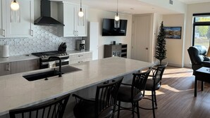 A modern kitchen with a central island, dining chairs, a coffee machine, and pendant lighting. - New Luxury 3-Bedroom Condo 1/2 Block to Main St (Winter Park)