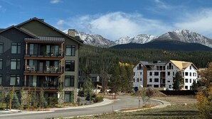 Un edificio de varios pisos con balcones, una carretera al frente y montañas nevadas en el fondo.