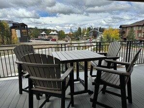 Eine Terrasse mit zwei Adirondack-Stühlen und einem Tisch, mit Blick auf einen Parkplatz und Gebäude.