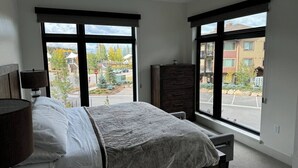 Un dormitorio con cama, cómoda y ventana con vistas a un estacionamiento y edificios.