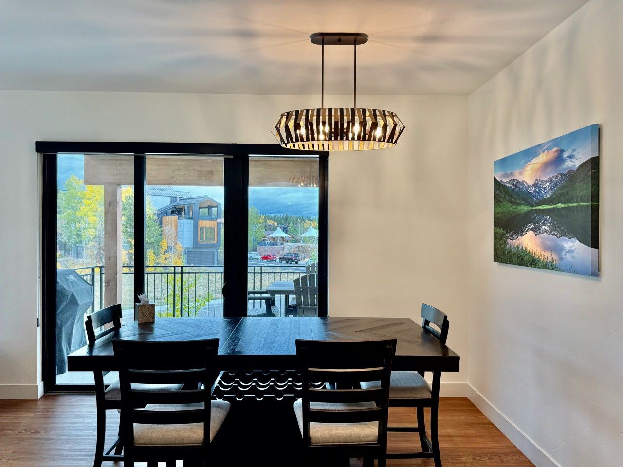 Un comedor con mesa y sillas, una lámpara colgante, un cuadro en la pared y vistas a través de un ventanal.