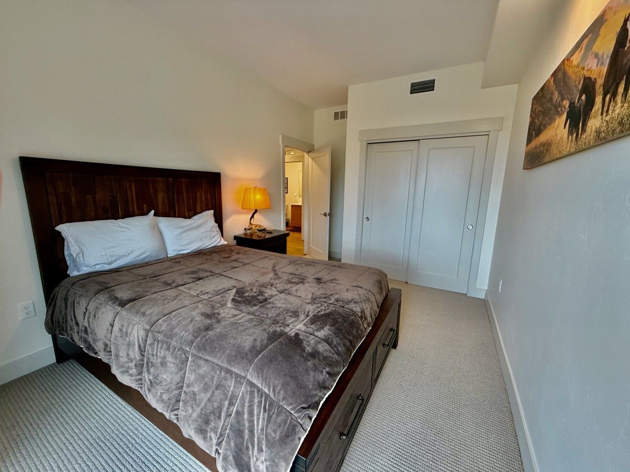A bedroom with a bed, nightstand, lamp, wardrobe, and a painting on the wall.