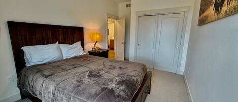 A bedroom with a bed, nightstand, lamp, wardrobe, and a painting on the wall.