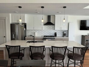 Una cocina moderna con una isla central, taburetes de bar, electrodomésticos de acero inoxidable e iluminación colgante.