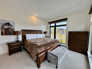 Ein Schlafzimmer mit einem großen Bett, einem Nachttisch, einer Kommode und einem Fenster mit Blick.