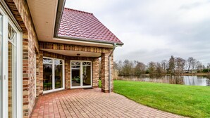 Une maison avec une façade en briques, un toit recouvert de tuiles rouges et un patio en briques menant à une entrée avec une porte vitrée.