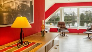 Una habitación con una pared roja, un escritorio de madera con una lámpara, una silla y una ventana con vista a un puente.