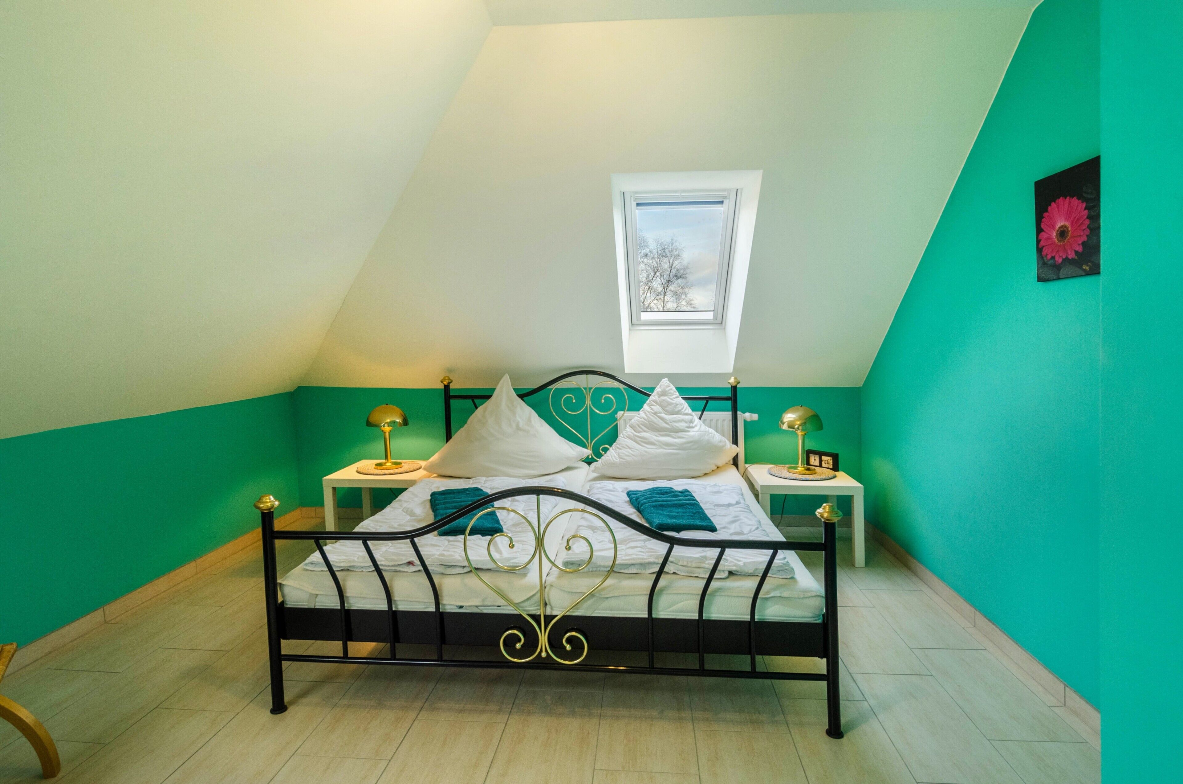 A bedroom with a sloped ceiling, a skylight, a bed with white bedding, two bedside tables with lamps, and a green wall.