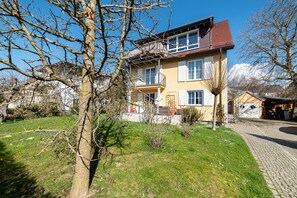 Une maison à deux étages avec un balcon, une allée pavée et une cour gazonnée.