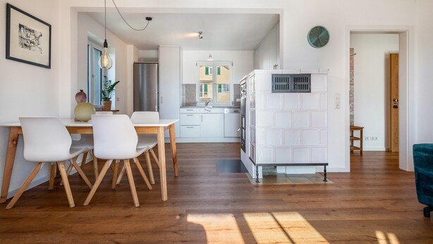 A modern kitchen with white cabinets, a dining area with a wooden table and chairs, and a view of the outside. - Apartment 'Windhager Seeblick' with Lake View, Balcony and Wi-Fi (Friedrichshafen)