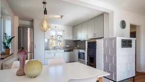 A modern kitchen with white cabinetry, a stainless steel refrigerator, a built-in oven, and a white dining table with chairs. - Apartment 'Windhager Seeblick' with Lake View, Balcony and Wi-Fi (Friedrichshafen)