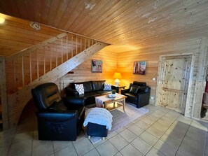 Un intérieur en bois avec un escalier, un ensemble de canapés en cuir noir, une petite table avec une lampe et une porte au design rustique.